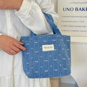 Détail du sac cabas en denim bleu avec broderies de nœuds blancs et patch logo