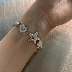 Silver metal charm bracelet with star and heart pendants worn on a model wrist