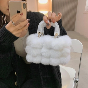 Chic white faux fur handbag with leather handles and gold rings in a handheld mirror view