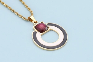 Detail of round pendant with magenta gemstone and black-white enamel on golden twist chain