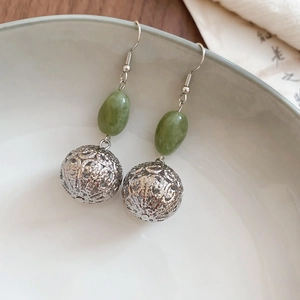 Détail de perles en résine verte et boules en métal argenté évidé sur boucles d'oreilles