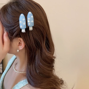Close-up of light blue teardrop hair clips with white daisy patterns on brown wavy hair