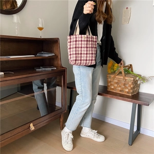 Detail of wool blend plaid bento bag with red checks and snap closure carried by a model