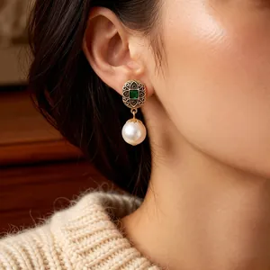 Vintage gold pearl drop earrings with green emerald stone on an elegant model