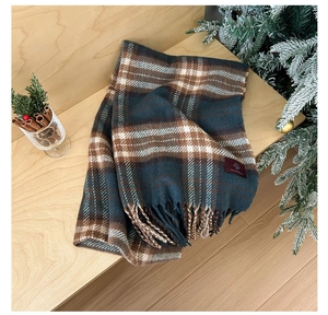 Close-up of classic plaid scarf with fringe edges and red woven label on wood surface