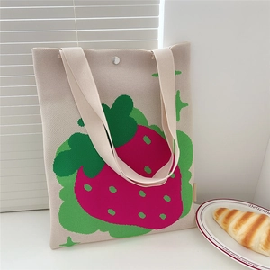 Close-up of beige knitted tote bag with pink strawberry patterns and snap button closure