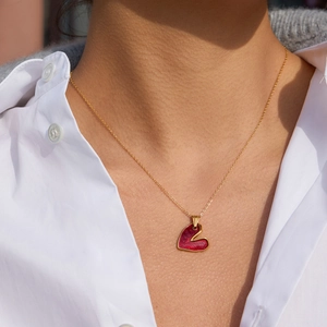 Dettaglio di una collana dorata con ciondolo a cuore rosso indossata da una modella