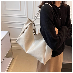 Side view of a creamy white oversized faux leather tote bag worn by a female model