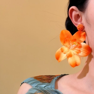 Primer plano de unos pendientes de flores de rafia naranja usados por una modelo.