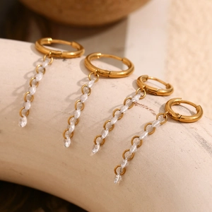 Close-up of 18K gold plated tassel earrings with white zircon on cream display stand