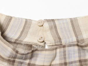 Detail of plaid cropped top showing beige and brown check fabric with dual buttons