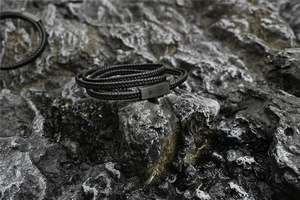 Nahaufnahme eines mehrlagigen schwarzen Lederarmbands auf dunklem Felsenhintergrund