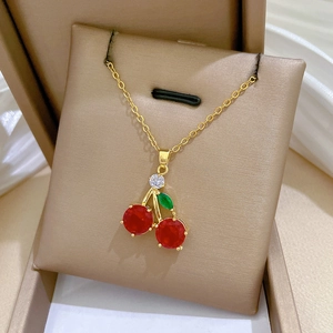 Titanium steel cherry pendant necklace with red crystals and gold chain on beige box