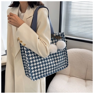 Detail of blue houndstooth tote bag featuring soft white pom-poms and leaf embroidery