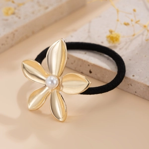 Detailed shot of a golden flower hair tie with a white pearl on a stone tray