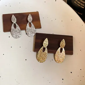 Polished gold and silver drop earrings with textured mosaic pattern on wooden stand