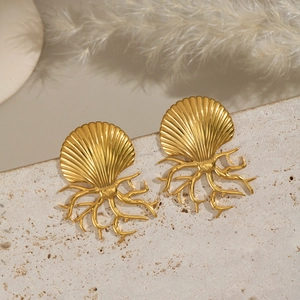 Detail of gold shell and coral branch stud earrings on a textured stone surface