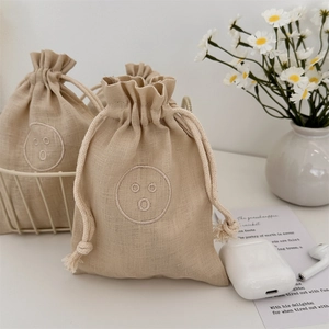 Close-up of linen drawstring bag featuring a minimalist embroidered smiley face design