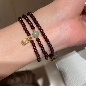 Detail view of triple-layer garnet bracelet with golden Fu pendant and green accent bead