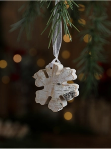 Detail of snowflake-shaped natural wood Christmas ornament hanging with white ribbon