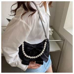 Detail of black fabric shoulder bag featuring a large bow and pearl chain strap