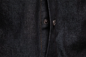 Macro shot of twill denim fabric texture with contrast orange stitching and metal buttons
