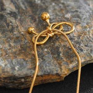 Macro di una collana dorata con pendente a fiocco appoggiata su una roccia scura