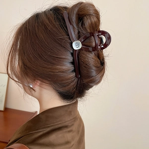 Detail of dark brown resin hair claw with CD logo metal plaque on elegant updo hair