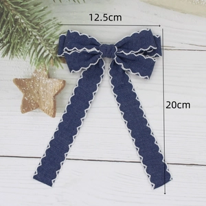Detail view of a 12.5cm denim ribbon bow hairpin with white wavy embroidered edges