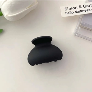 Detailed top view of a matte black mini hair claw clip on white background with floral decor