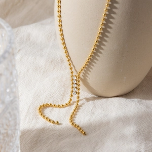 Détail d'un collier en Y à billes dorées avec quatre zircons sur un vase en céramique
