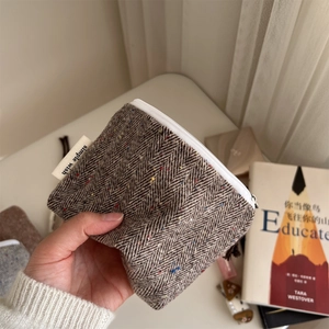 Handheld view of a mini herringbone tweed pouch with colorful flecks and a zipper closure