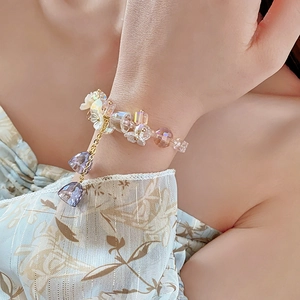 Detail of pink crystal flower bracelet with purple bell charms on a golden chain
