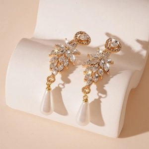 Detail of gold leaf earrings with sparkling crystals and teardrop pearl on white stand