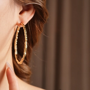 Gros plan d'une grande boucle d'oreille créole dorée martelée portée par un mannequin