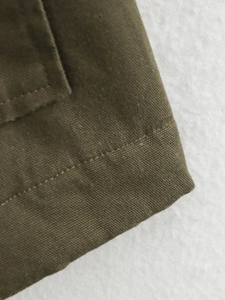 Detail shot of army green canvas texture and reinforced double-row stitching on the jacket