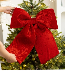 Close-up of hands placing a large red velvet bow on top of a decorated Christmas tree