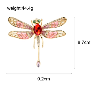 Oversized dragonfly brooch with pink wing crystals and red main stone on white background