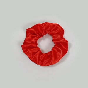 Close-up of bright red satin scrunchie showing detailed silk texture and pleats