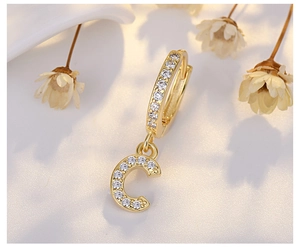 Macro detail of gold C-letter huggie earring encrusted with sparkling cubic zirconia