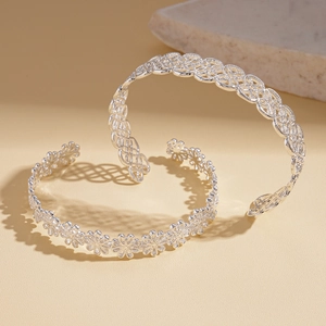 Close-up of silver hollow floral and geometric woven open bangles on a warm beige surface
