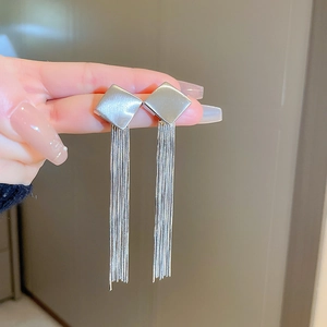 Detail of silver tassel drop earrings with rhombus metallic studs held by hand