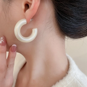 Close-up of creamy white C-shaped acrylic hoop earrings with a glossy pearl-like finish