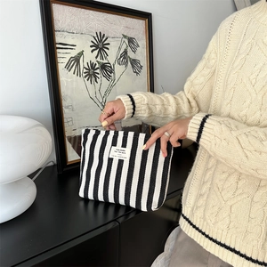 Detail of a large capacity striped canvas toiletry bag held in hands on a black desk