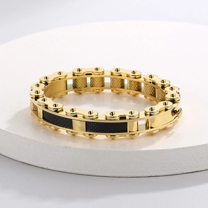 Detail of gold curb chain bracelet with black carbon fiber inlay on white pedestal