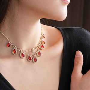 Detail of gold necklace with pear-cut red gemstone and sparkling rhinestones on model