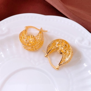 Detail of 18K gold plated hollow hoop earrings with a 3D flower on a white porcelain dish
