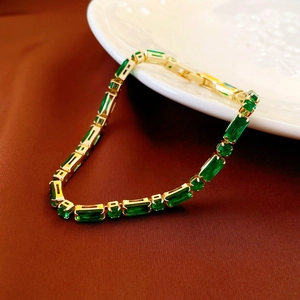 Close-up of green rectangular zircon and gold plated link bracelet on white porcelain