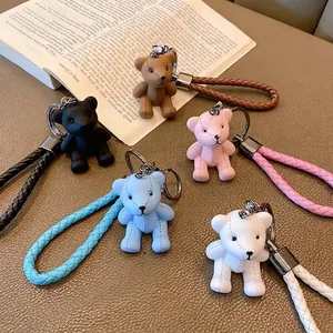 Five colored leather teddy bear keychains with woven straps and metal rings on a desk