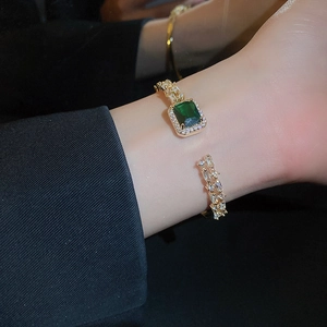 Close-up of golden open bangle featuring a rectangular emerald green gemstone and zircons